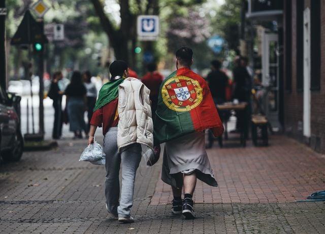 Two people walking down a city street, one draped in a Portuguese flag.