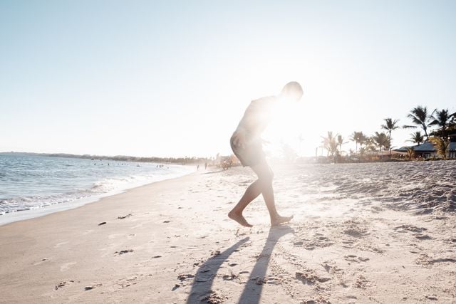 Person walking barefoot along a sandy beach at sunset.